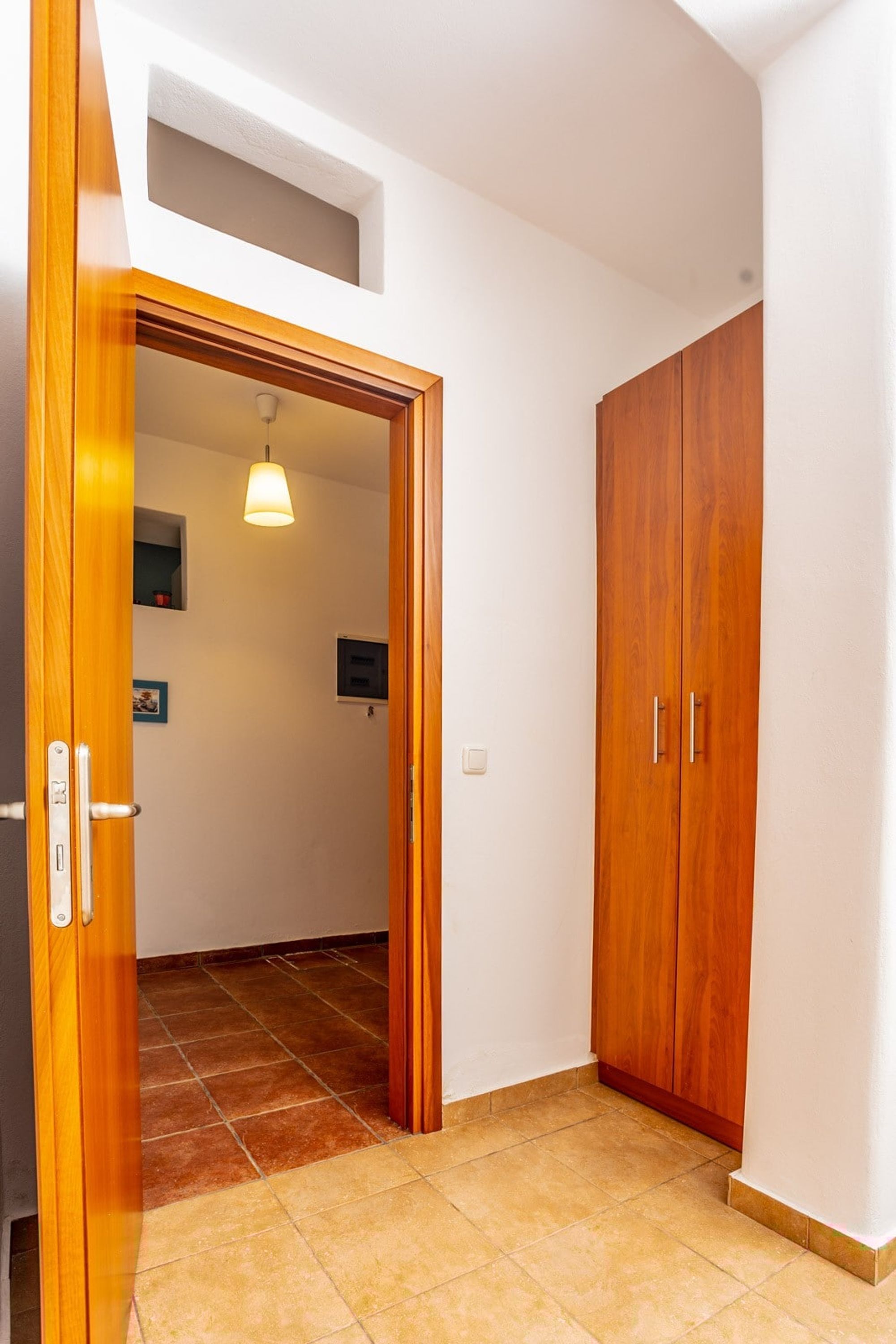 A hallway with a wooden door, a wardrobe, and a tiled floor.