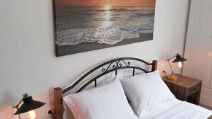 Une chambre à coucher avec un lit, deux tables de chevet avec des lampes, un climatiseur fixé au mur et un tableau représentant un coucher de soleil au-dessus du lit.