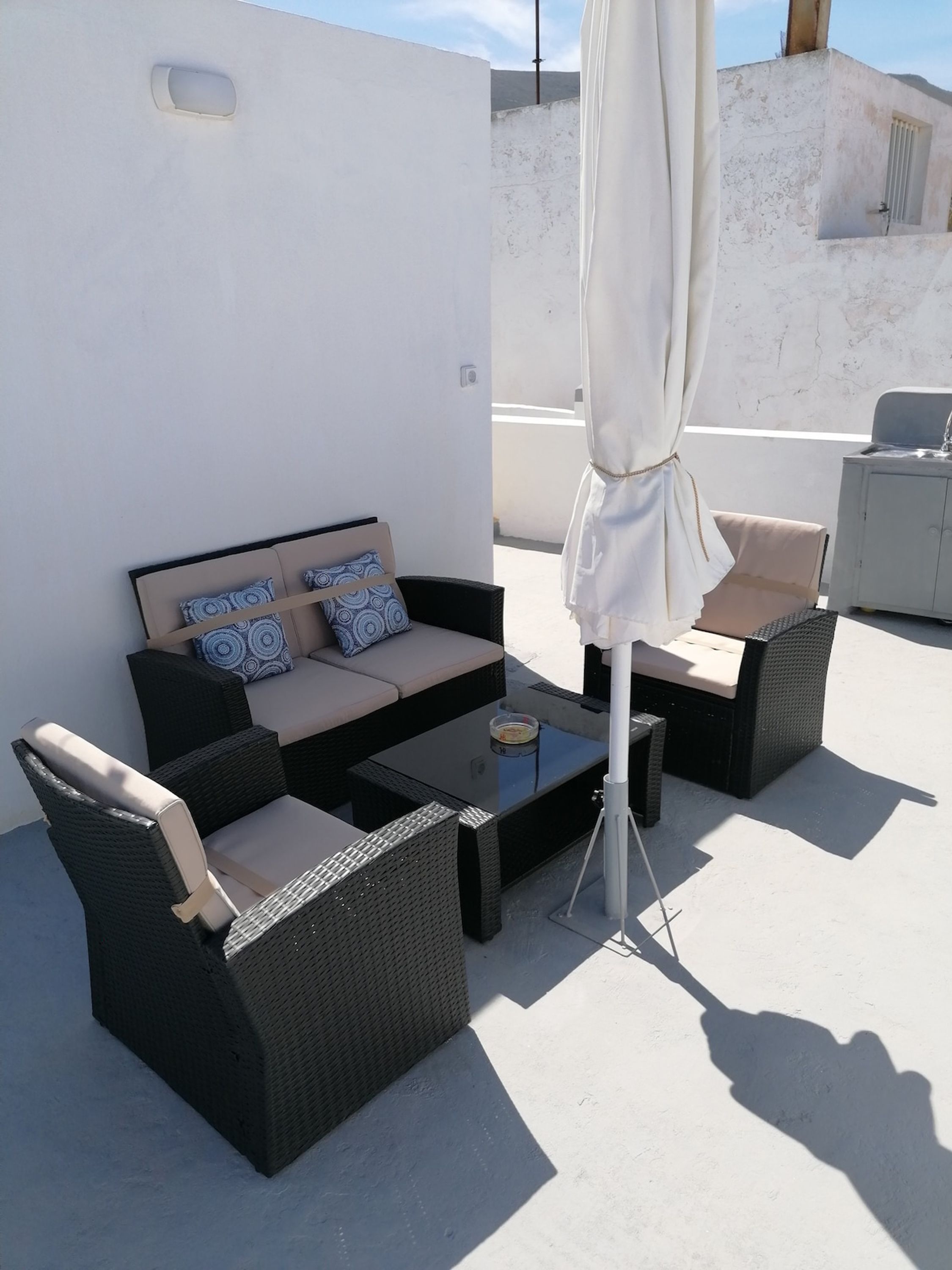 Un espace extérieur aménagé avec des meubles en osier, un parasol blanc et une vue sur le paysage.