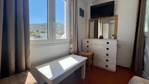 Une chambre à coucher avec un lit, un bureau, une commode, un téléviseur et une fenêtre avec des rideaux.