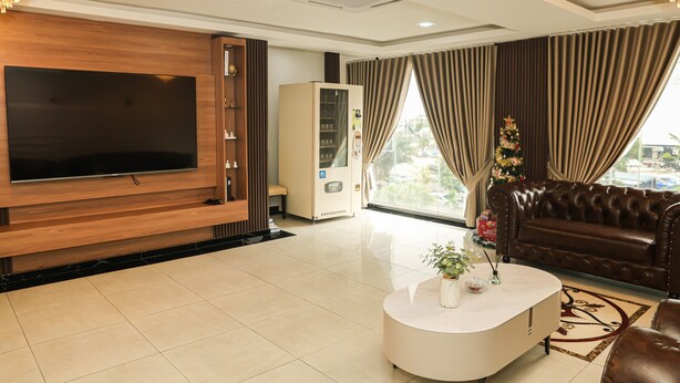 A modern living room with a flat-screen TV, a coffee table with decorative items, a leather sofa, a vending machine, and a Christmas tree. - De Royal Hotel (Ampang)