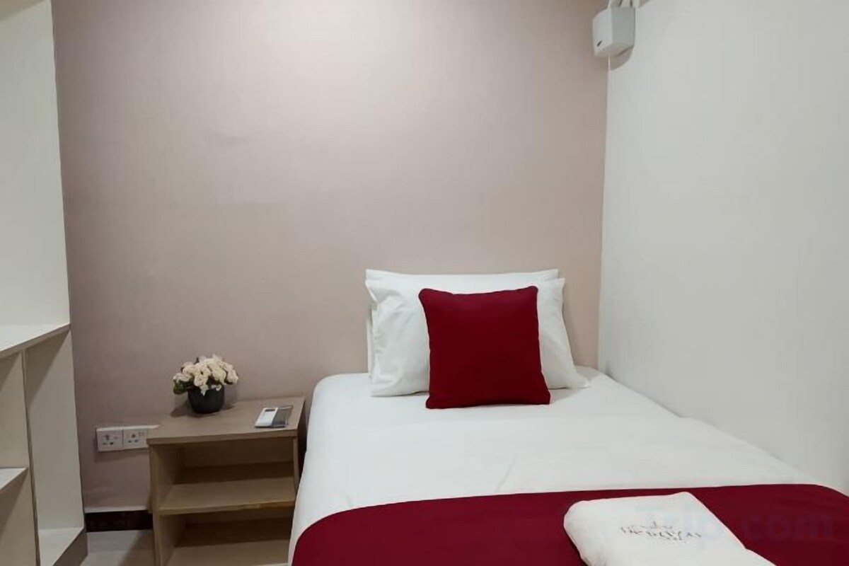 A hotel room with a bed, a nightstand, a vase with flowers, and a red throw blanket.