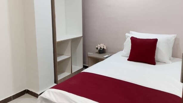 A hotel room with a bed, a wardrobe, a nightstand with a vase of flowers, and a red throw blanket. - De Royal Hotel (Ampang)