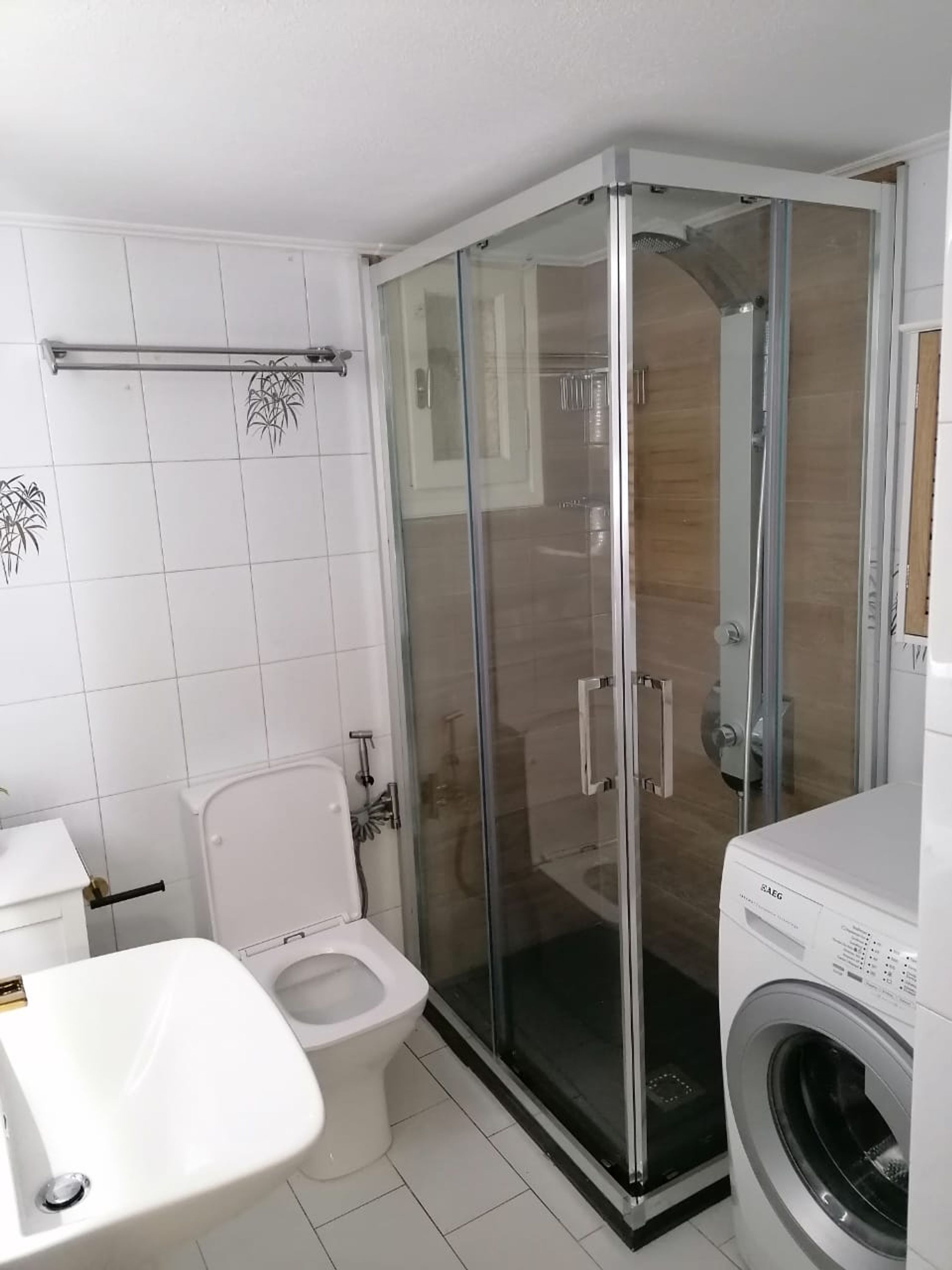 A modern bathroom with a glass-enclosed shower, a toilet, and a washing machine.