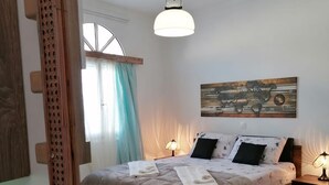 A bedroom with a large bed, two bedside lamps, a world map artwork on the wall, and a window with curtains. - Studio Orion - Allparos Villas (Paros)