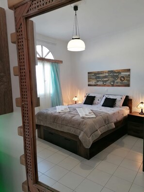 A bedroom with a large bed, two bedside lamps, a world map artwork on the wall, and a window with curtains. - Studio Orion - Allparos Villas (Paros)