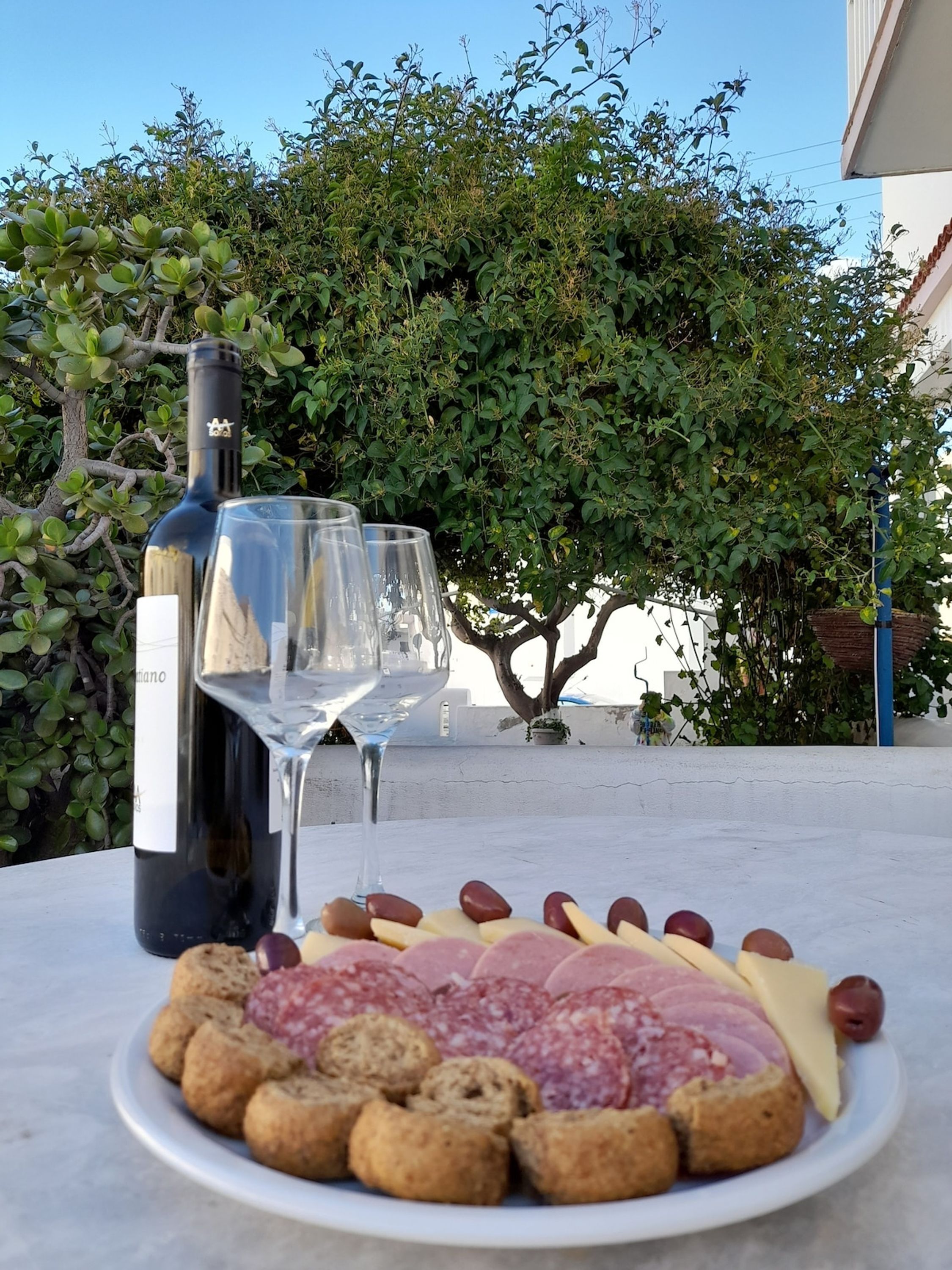 A table with a wine bottle, glasses, and a plate of food.
