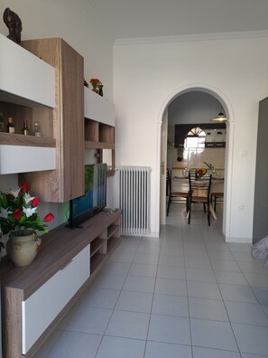 A modern living room with a TV, wooden shelves, and a vase of flowers. - Studio Orion - Allparos Villas (Paros)