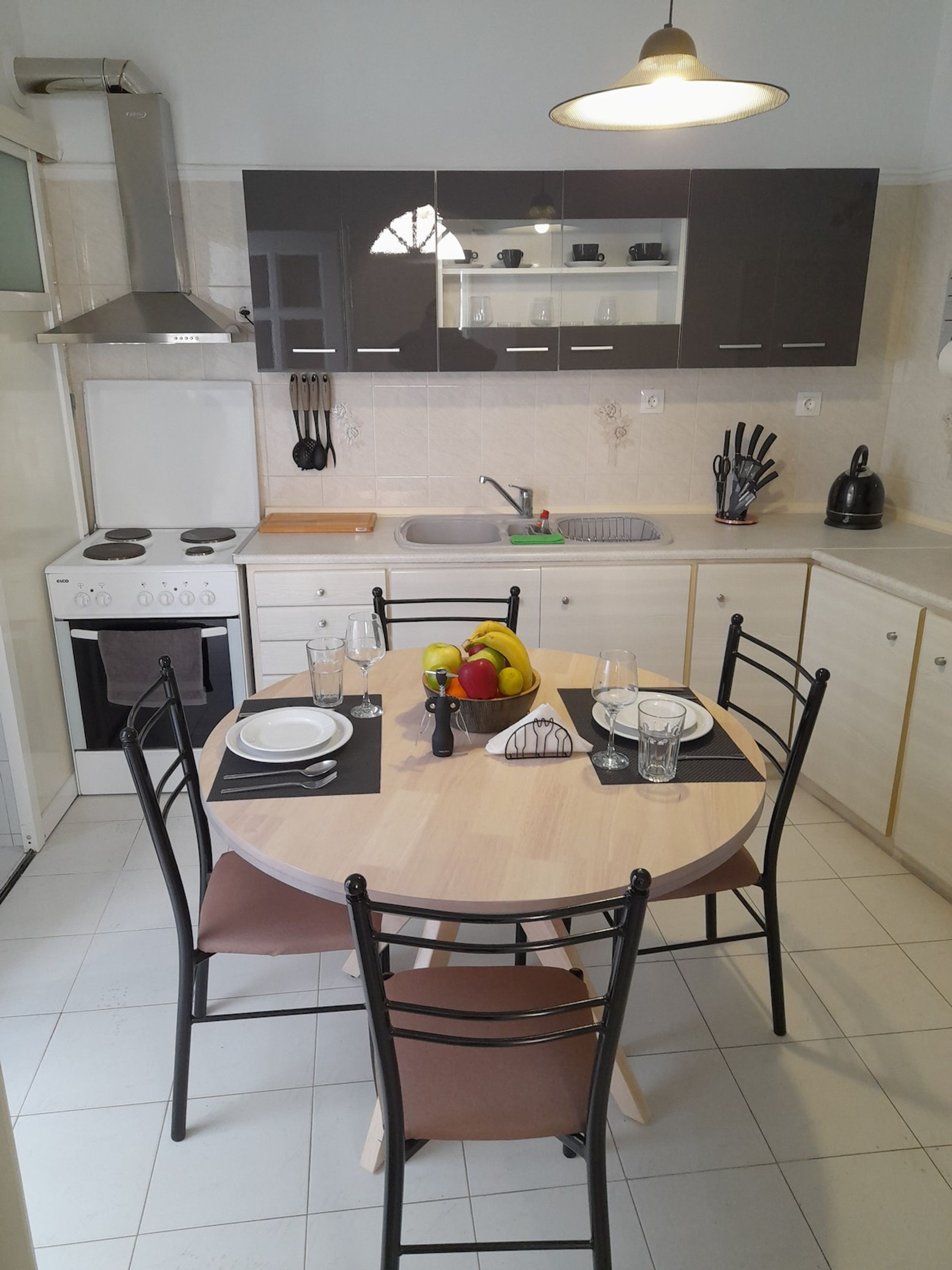 Een moderne keuken met een eettafel voor vier personen, compleet met stoelen, een fruitschaal en een waterkoker.