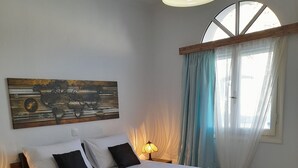 Una cama bien hecha con sábanas blancas y dos toallas dobladas, un cuadro de un mapa mundial en la pared, una lámpara de noche y una ventana con cortinas translúcidas.