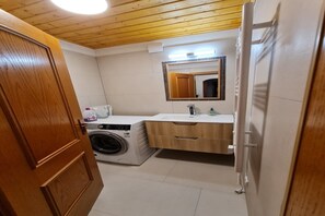 Een wasserij met een wasmachine, een wasbak en een spiegel.