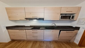 A kitchen with light wood cabinets, a black countertop, a stainless steel microwave, and a sink. - Cozy Apartment with mountain view (Bad Kleinkirchheim)