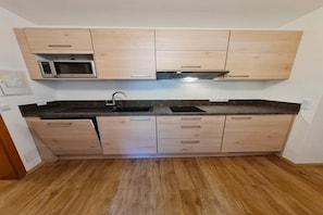 A compact kitchen with wooden cabinets, a microwave, a sink, and a stainless steel range hood.