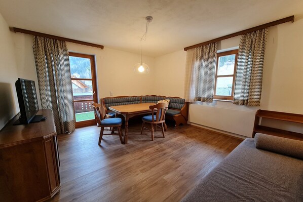 Una habitación acogedora con una mesa de madera, sillas, un sofá y un televisor sobre un mueble.