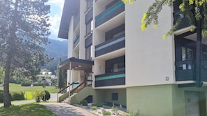 A multi-story building with a green and white facade, a staircase leading to the entrance, and a view of a mountainous landscape in the background.