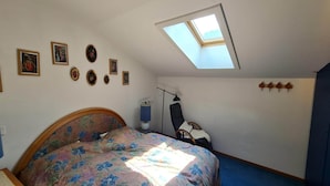 A bedroom with a skylight, a bed with floral bedding, a chair, and wall-mounted decorations.