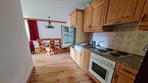 Een keuken met houten kastjes, een fornuis en een eethoek met een tafel en stoelen.