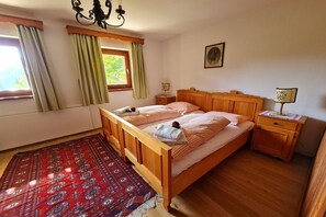 Ein Doppelbett mit Holz-Kopfteil, zwei Nachttische, ein rot gemustertes Teppich, ein Fenster mit Vorhängen und ein Wandbild.