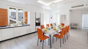 Eine moderne Küche mit weißen Schränken, ein Essbereich mit orangefarbenen Stühlen und einer Kristallleuchtre.