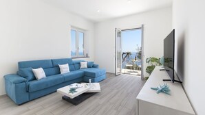 Ein modernes Wohnzimmer mit einem blauen Ecksofa, einem weißen Couchtisch und einem Fernsehgerät auf einem weißen Schrank.