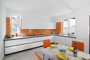 A modern kitchen with white cabinets, a black countertop, and orange accents. There is a dining table set with yellow plates, wine glasses, and a bottle of wine.