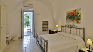 A bedroom with a bed, bedside lamps, a small table, a shelf with books, and a colorful painting on the wall. - Relax Star House. An oasis of peace in the heart of Salento (Presicce-Acquarica)