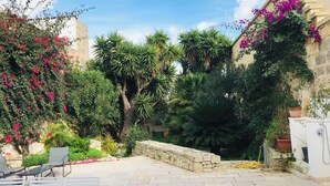 An outdoor patio area with a table and chairs, surrounded by lush greenery and flowering plants. - Relax Star House. An oasis of peace in the heart of Salento (Presicce-Acquarica)