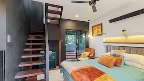 Une chambre moderne dotée d’un escalier en bois intégré, d’un grand lit avec une literie aux couleurs vives, d’une tête de lit avec éclairage intégré et d’une vue sur un espace extérieur accessible par une porte en verre.