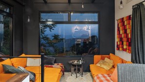 Un salon moderne avec des canapés orange, une petite table sur laquelle sont posées des bouteilles, et une grande fenêtre donnant sur l’extérieur.