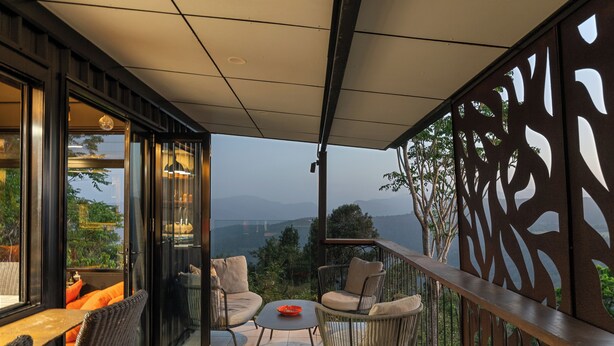 Un balcon agrémenté de meubles en osier, d’une table en verre et offrant une vue sur les montagnes.