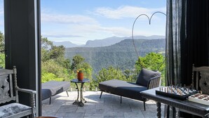 A balcony with a sofa, a small table, and a chessboard, overlooking a mountainous landscape.