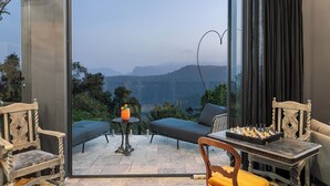 A room with a view of mountains, a chess table, a sofa, and a chair.