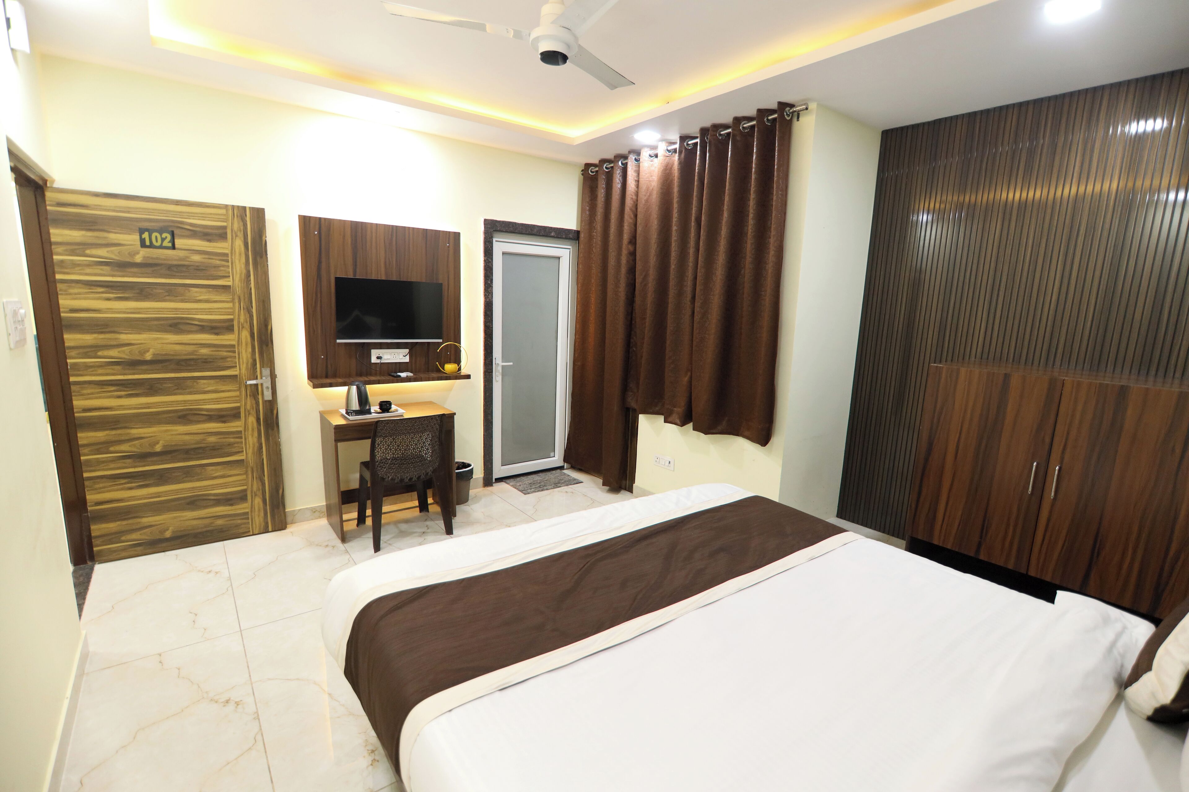 A hotel room with a bed, desk, television, wardrobe, and a door marked with the number 102.