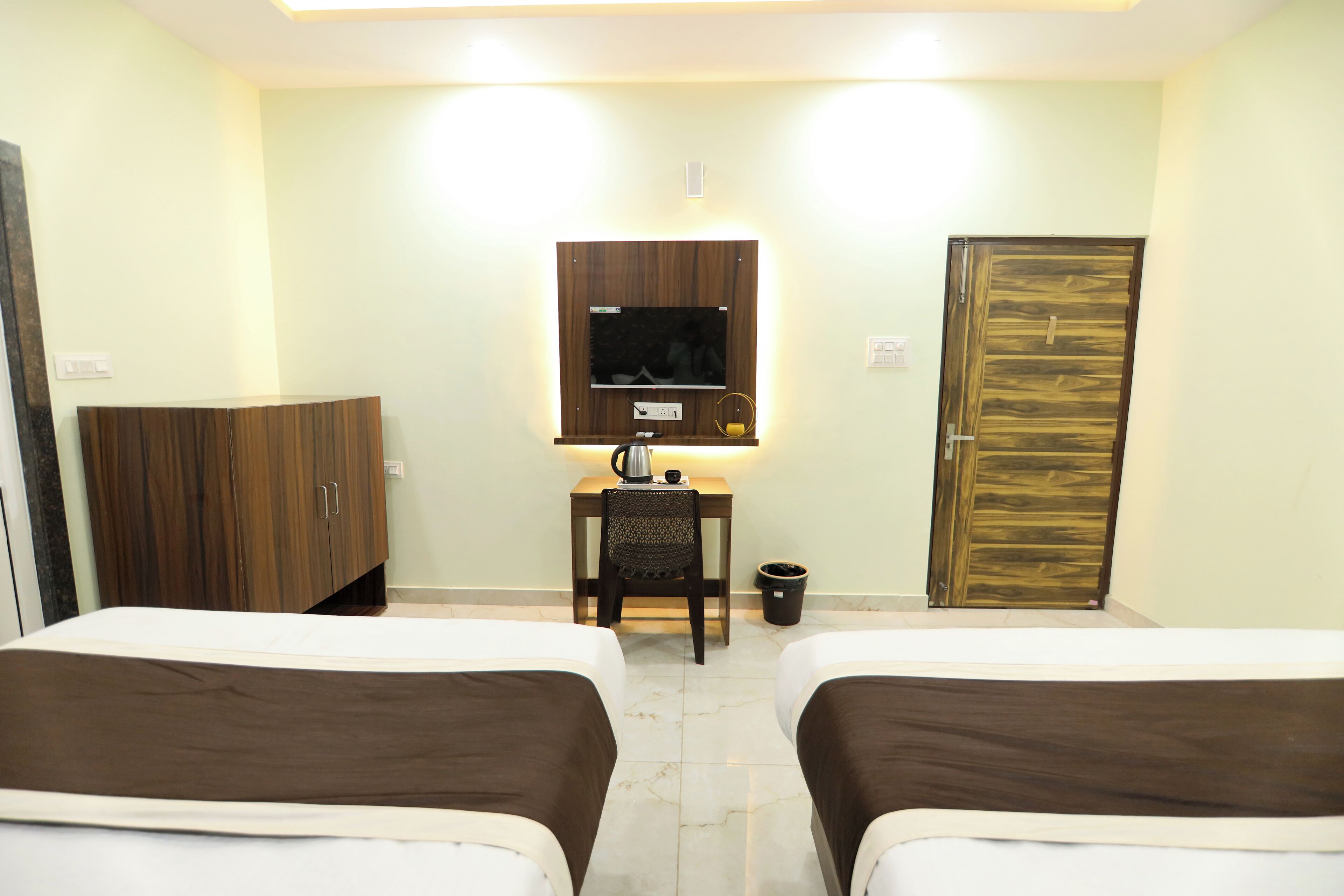 A hotel room with two beds, a television on a wooden stand, a desk with a chair, and a door.