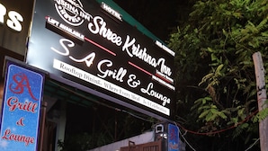 Een hotelingang met een bordje waarop 'Krishna Inn' en 'S.A Grill & Lounge' staan.