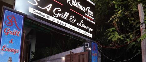 Entrada de un hotel con un letrero que dice 'Krishna Inn' y 'S.A Grill & Lounge'.