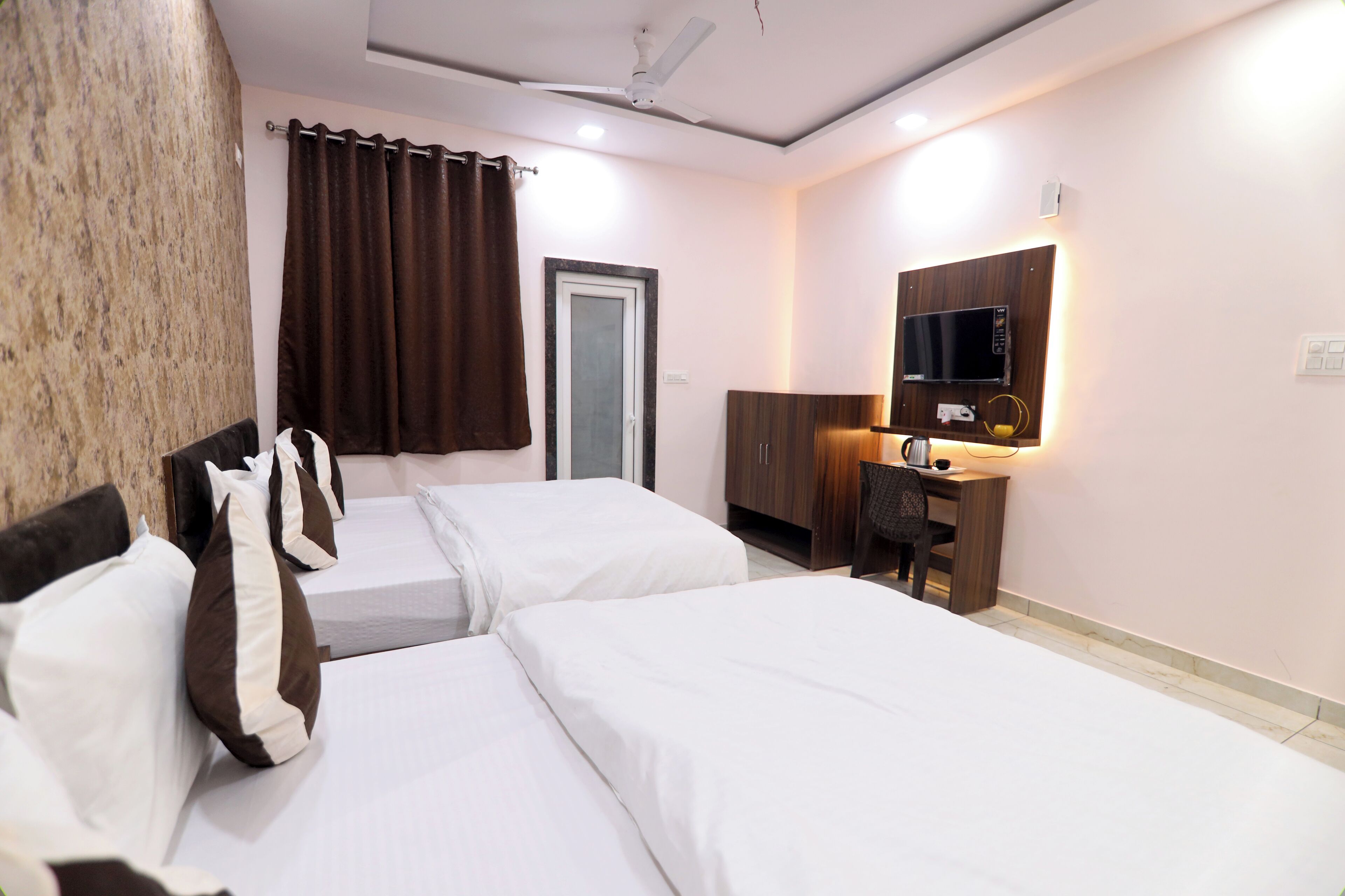 Una habitación de hotel con dos camas, un escritorio con computadora, televisión y ventilador de techo.
