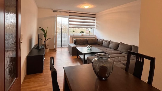 Een moderne woonkamer met een houten eettafel, een bank en een groot raam.