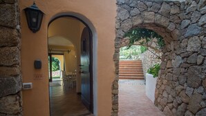 A corridor with a stone archway leading to a staircase and a door with a number plate. - Cosy apartment for 4 people with WIFI, A/C, pool and TV (Porto Cervo)