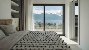 Ein Schlafzimmer mit einem großen Bett, Blick auf Berge und einen See, sowie eine Schiebetür, die auf einen Balkon führt.