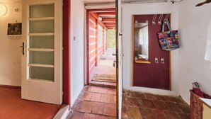 Un couloir avec une porte rouge, un miroir et un panier sur le côté droit.