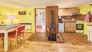 Une cuisine de taille modeste, dotée d’un poêle en briques, de meubles en bois et d’un coin repas avec une table et des chaises.