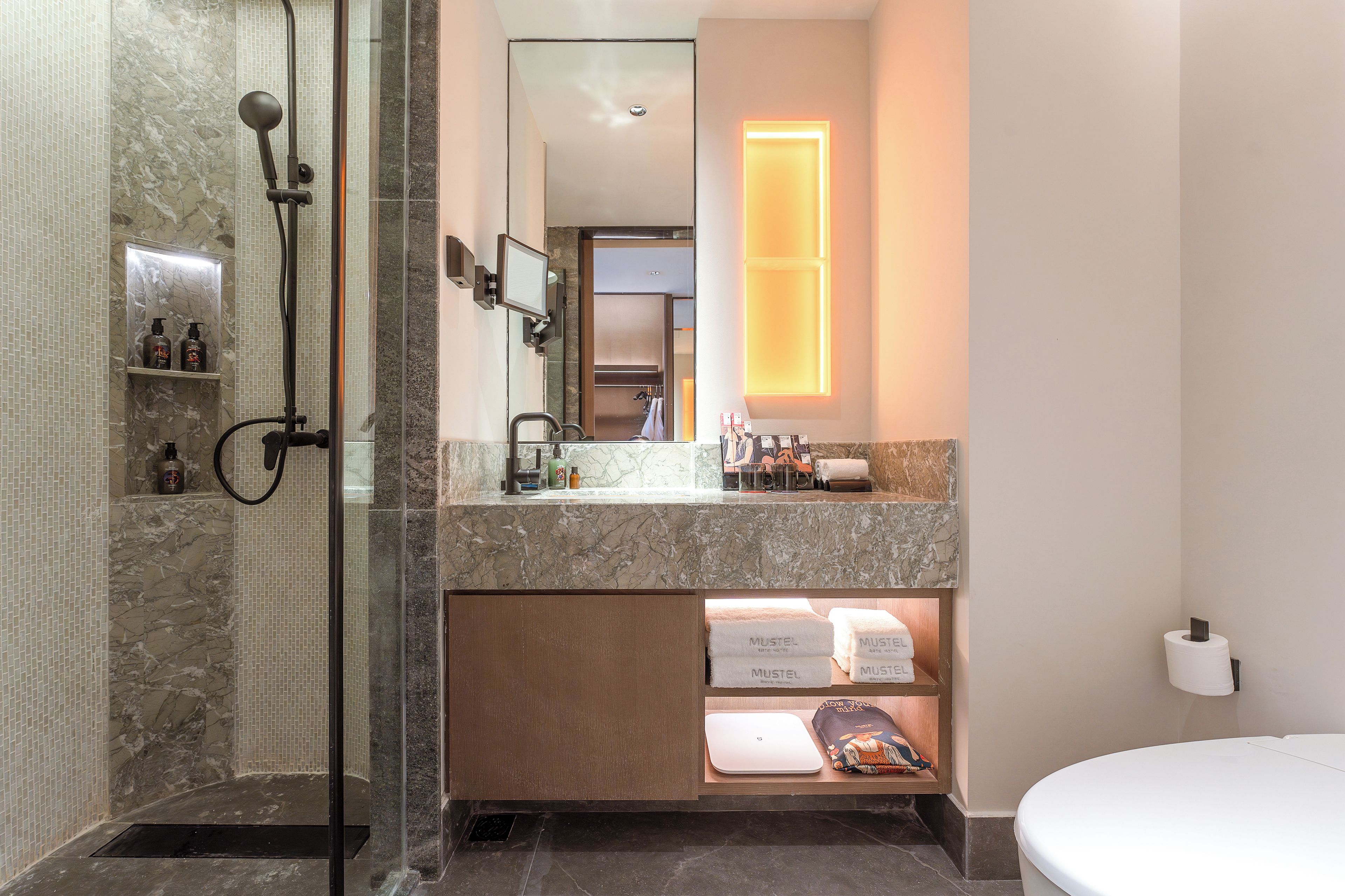 A modern bathroom with a glass-enclosed shower, a marble sink, and a built-in shelf with toiletries.
