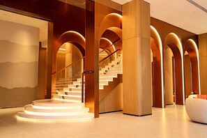 Eine moderne Hotelhalle mit einer zentralen Treppe, Holzsäulen und einer Sitzecke.