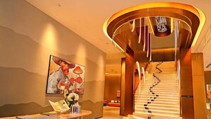 A modern hotel lobby with a spiral staircase, a reception desk, and a large painting of a man with mushrooms. - MUSTEL  ARTE  HOTEL  ZHENLIN  CHENGDU (Chengdu)