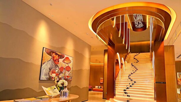 En moderne hotellobby med en spiraltrappe, en receptionsdisk og et stort maleri af en mand med svampe.