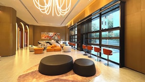 A modern lobby with a marble reception desk, seating areas with orange and black ottomans, and large windows offering a view of the outside. - MUSTEL  ARTE  HOTEL  ZHENLIN  CHENGDU (Chengdu)