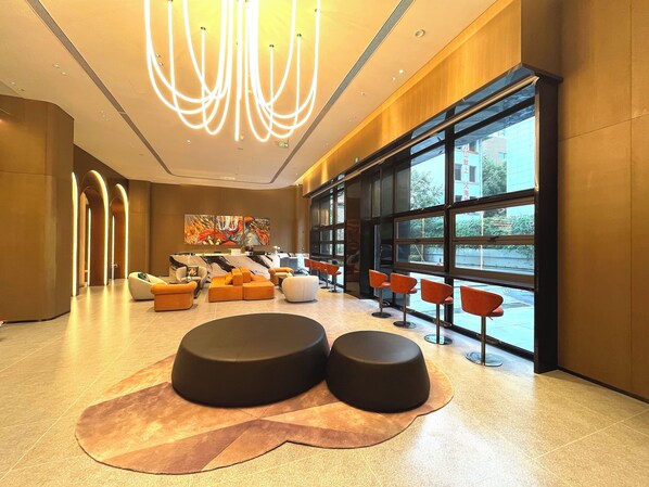 A modern lobby with a marble reception desk, seating areas with orange and black ottomans, and large windows offering a view of the outside. - MUSTEL ARTE HOTEL ZHENLIN CHENGDU (Chengdu)