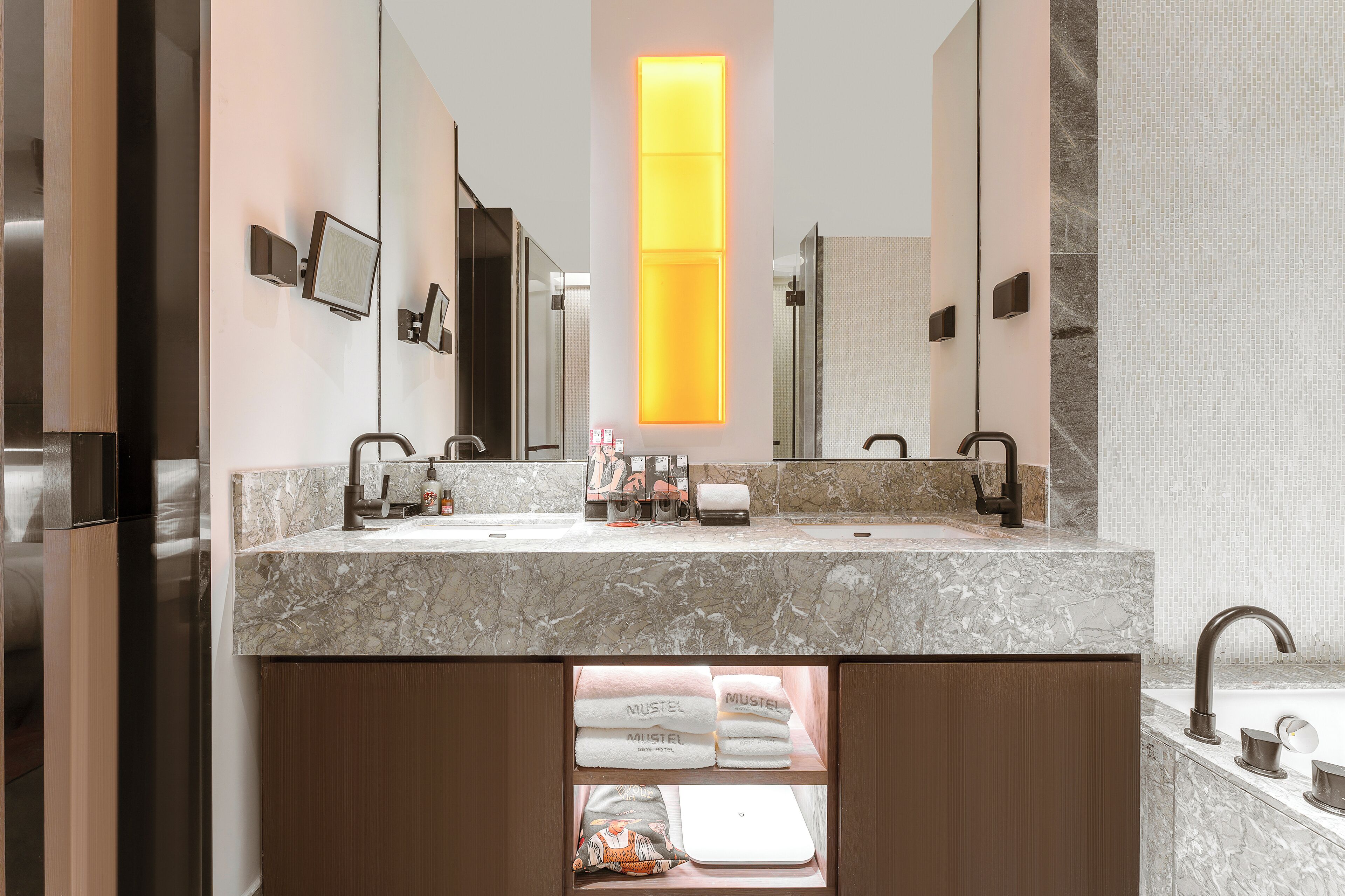 A modern bathroom with a marble countertop, dual sinks, a large mirror, and a vertical light panel.