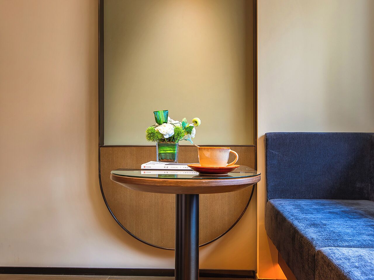 A round table with a book, a glass vase with flowers, and a cup.